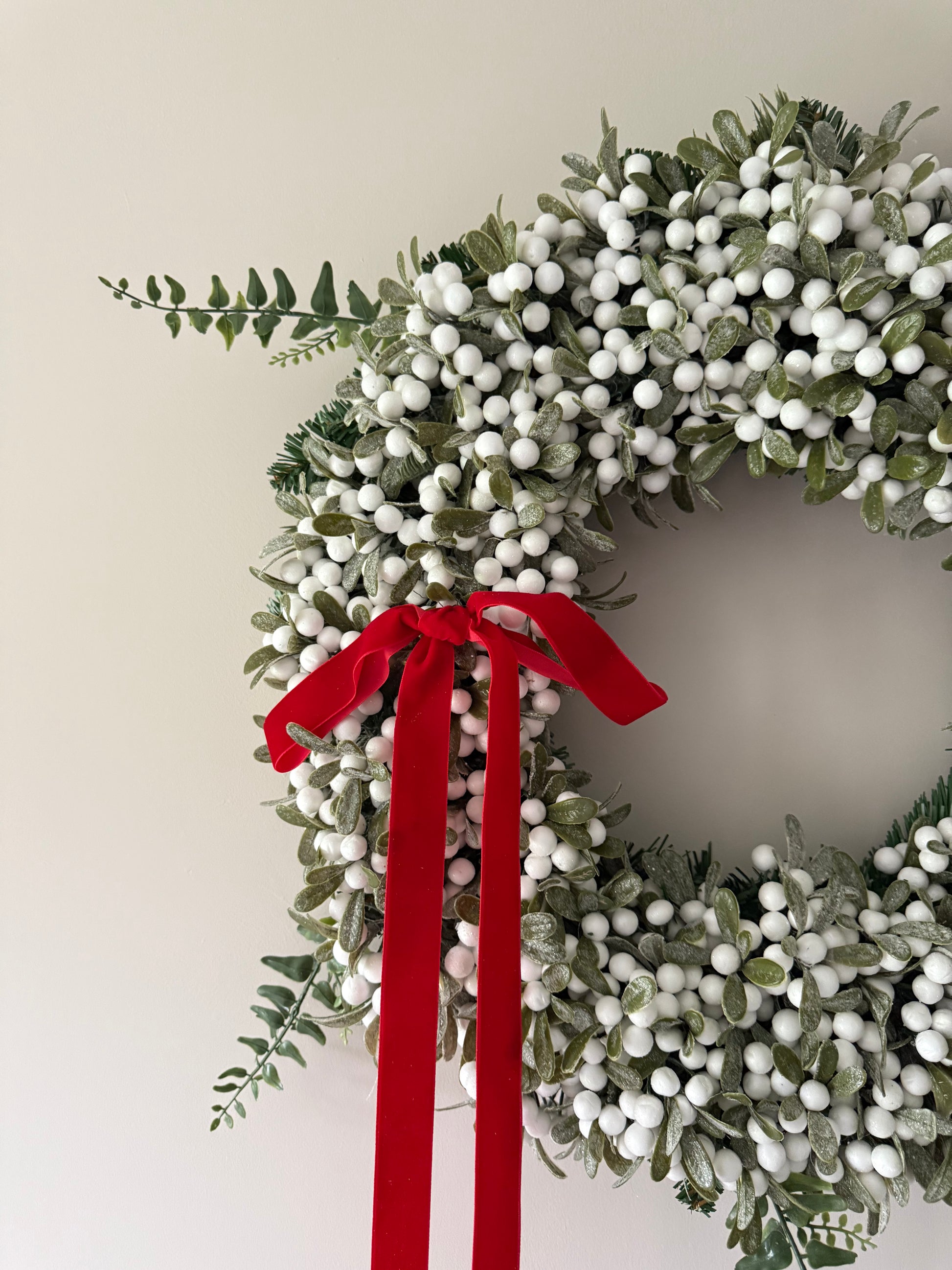 Christmas wreath with white berries and a red ribbon on a plain background