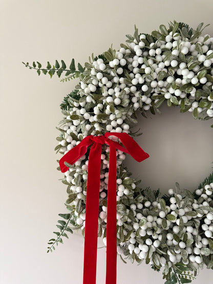 Christmas wreath with white berries and a red ribbon on a plain background