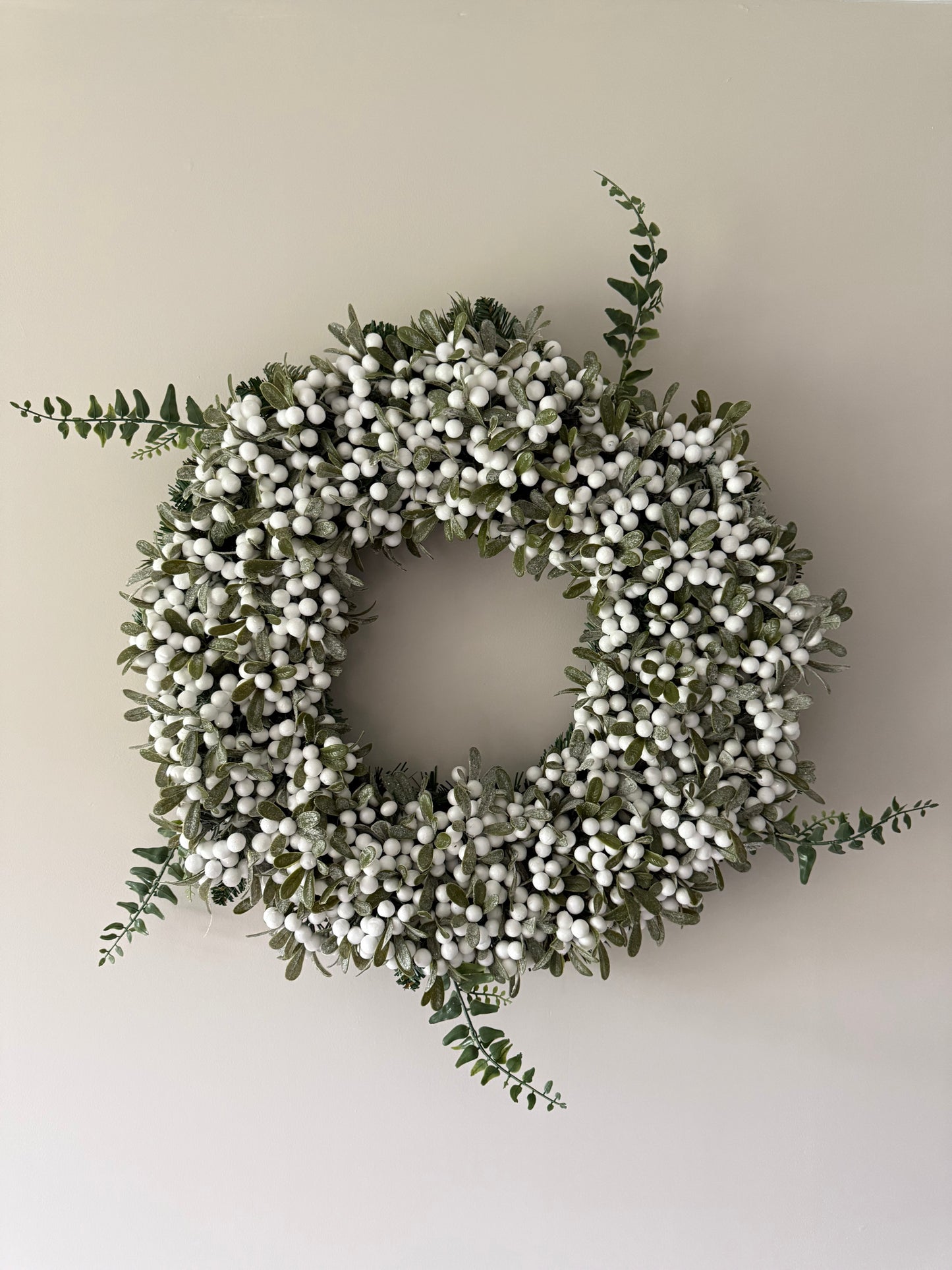 Decorative wreath with white berries and green leaves on a plain wall.