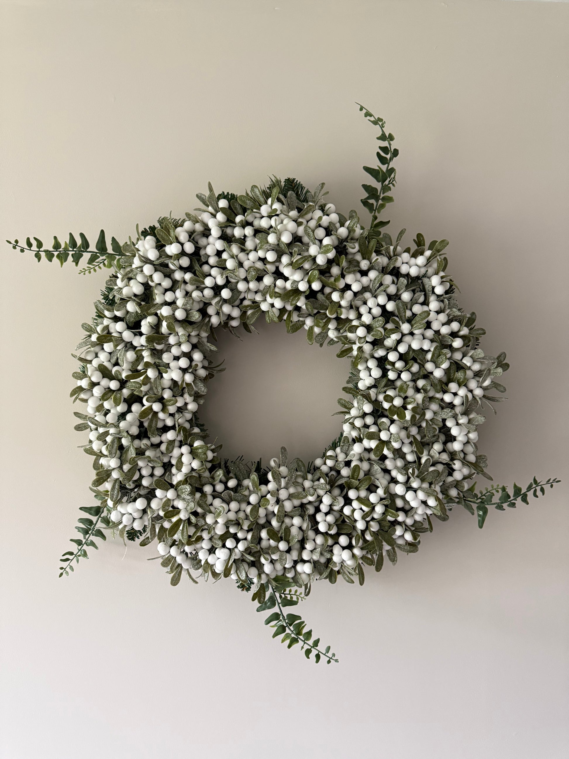 Decorative wreath with white berries and green leaves on a plain wall.