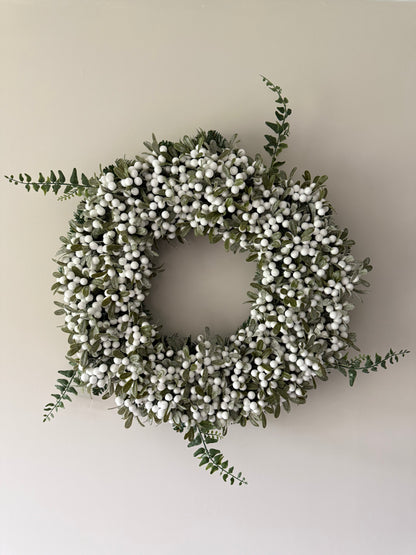 Decorative wreath with white berries and green leaves on a plain wall.
