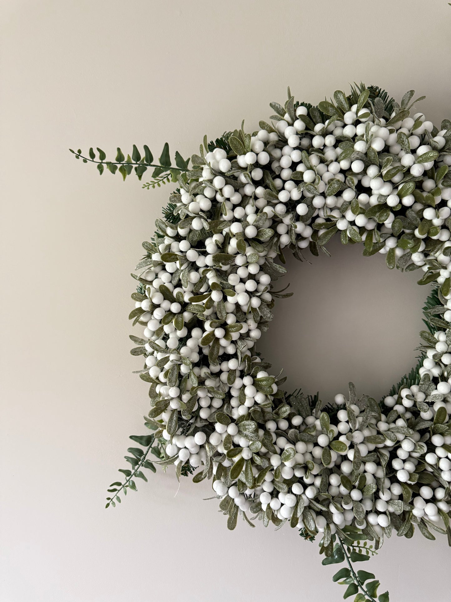 Decorative wreath with green leaves and white berries on a plain background