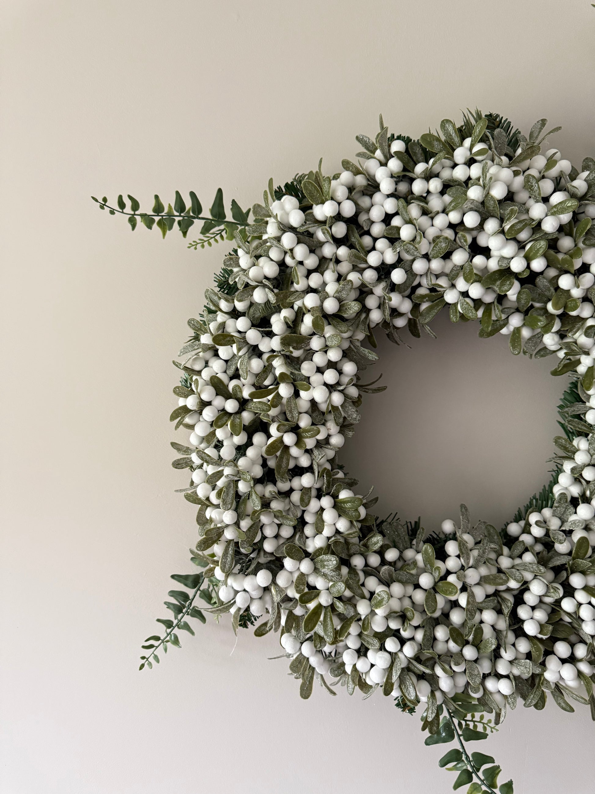 Decorative wreath with green leaves and white berries on a plain background