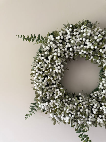 Decorative wreath with green leaves and white berries on a plain background