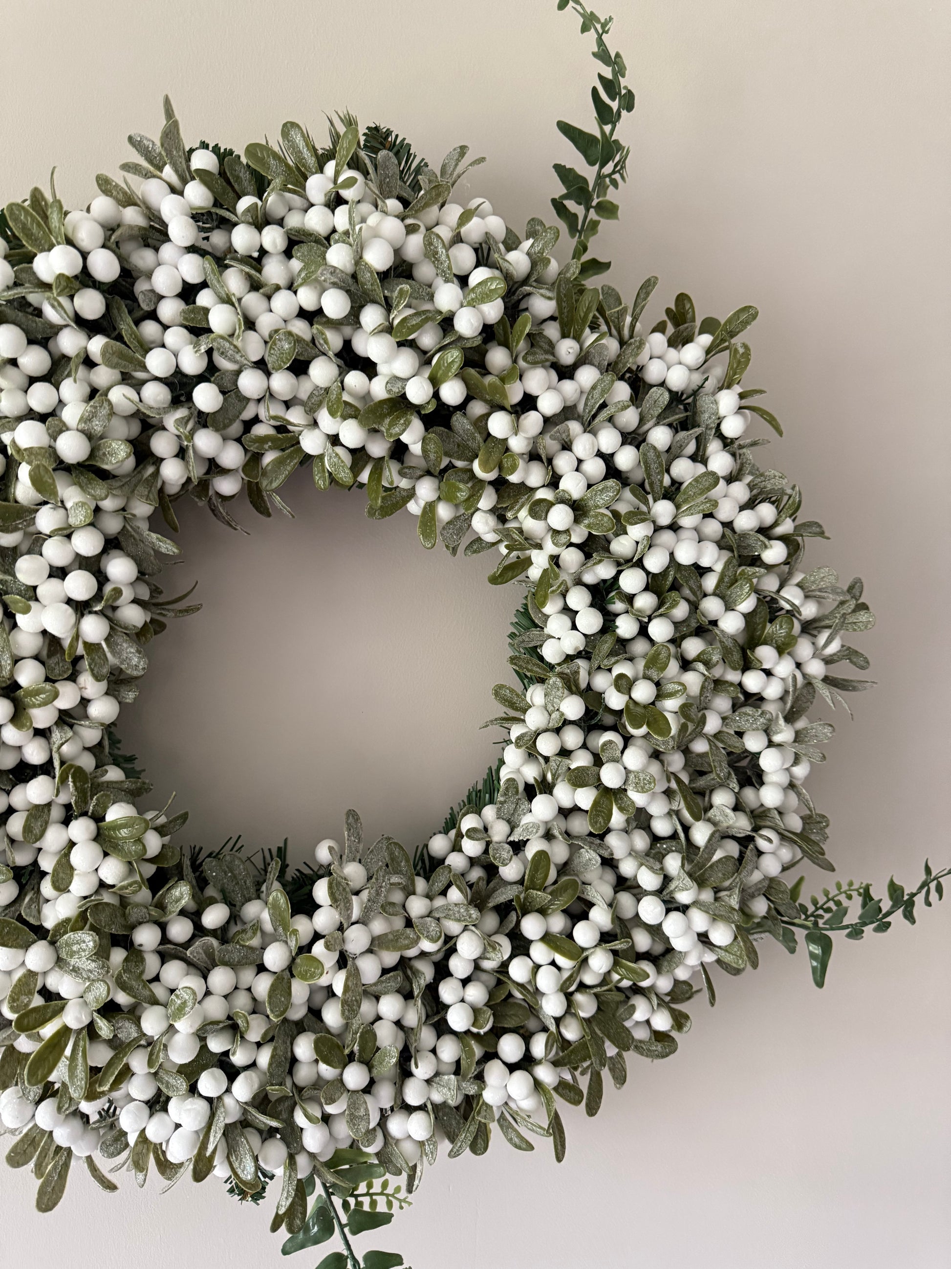 Decorative wreath with green leaves and white berries on a neutral background