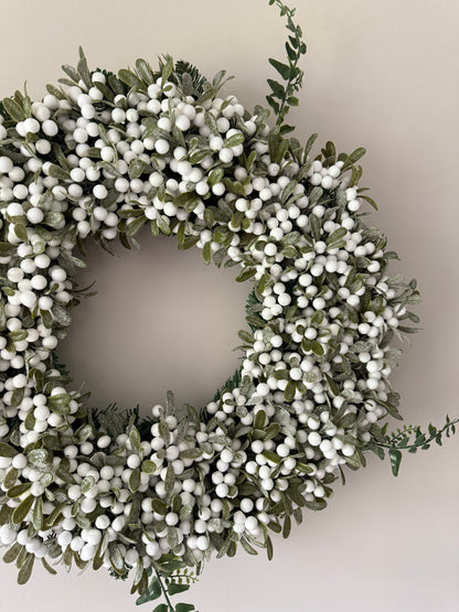Decorative wreath with green leaves and white berries on a neutral background