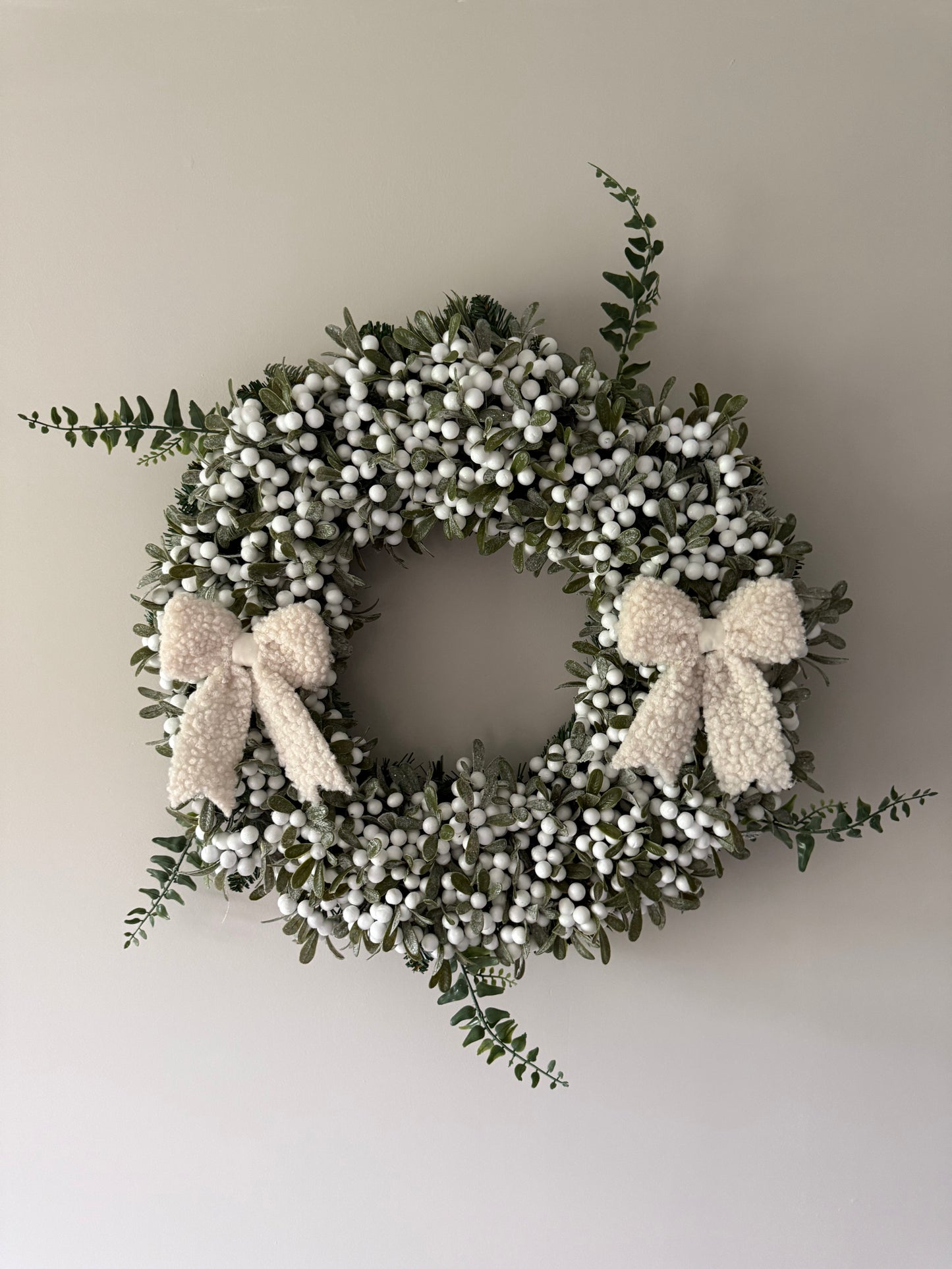 Decorative wreath with white berries and a bow on a plain wall