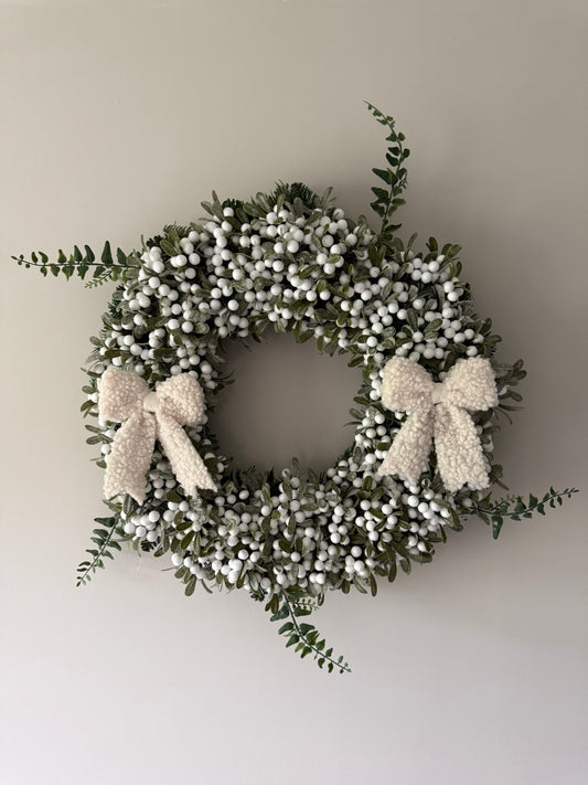 Decorative wreath with white berries and a bow on a plain wall