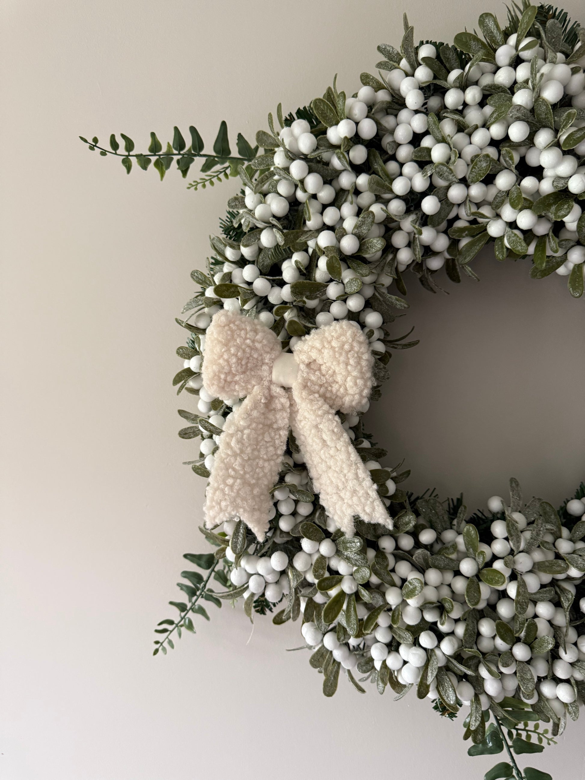 Decorative wreath with green leaves and white berries on a plain background