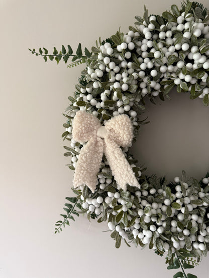 Decorative wreath with green leaves and white berries on a plain background