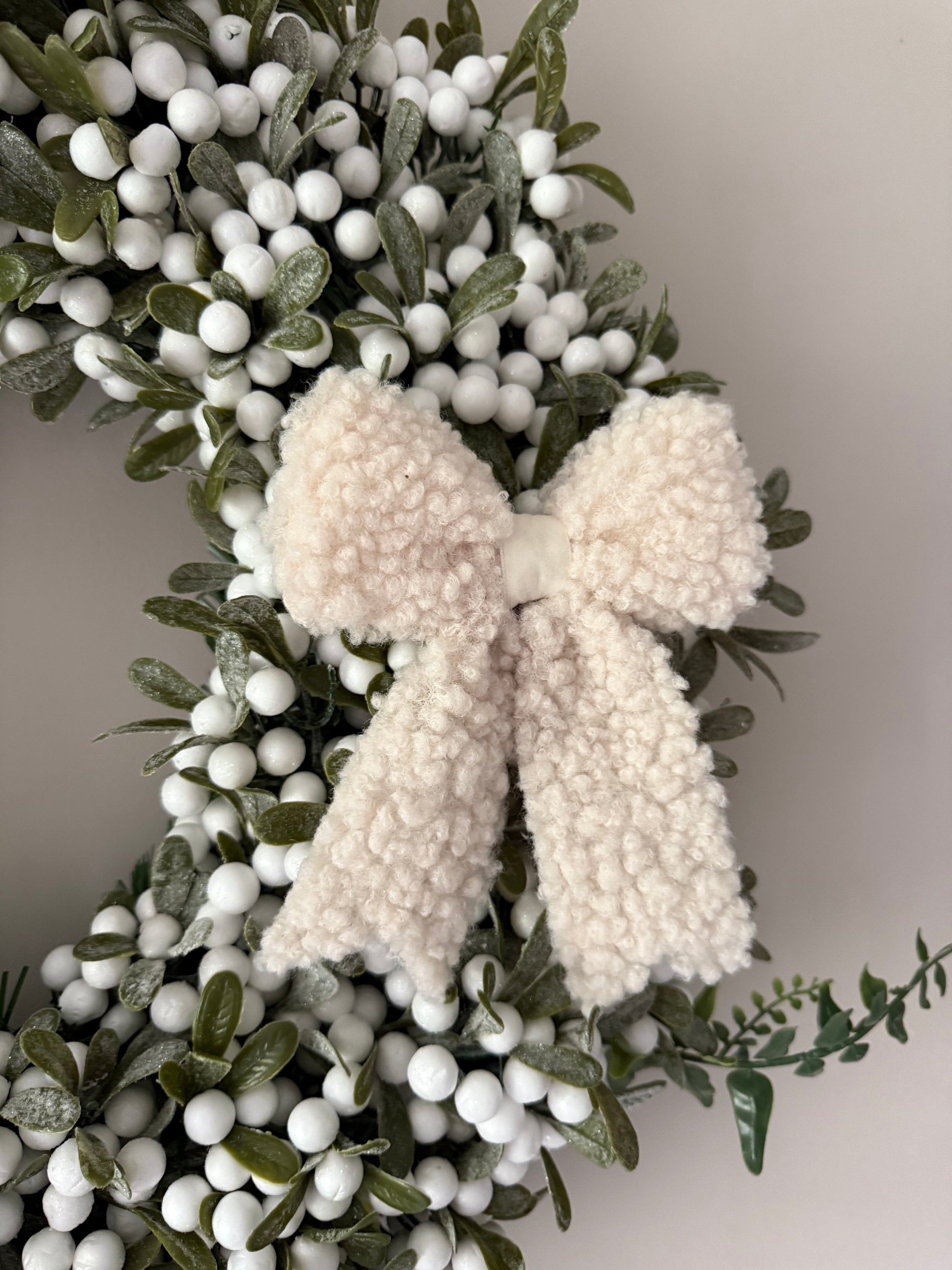 Decorative wreath with white berries and boucle bows on a plain background
