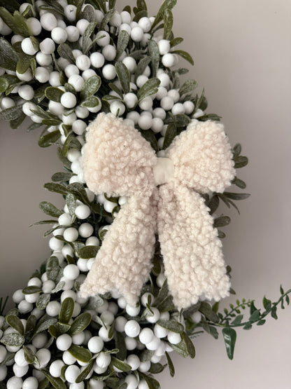 Decorative wreath with white berries and boucle bows on a plain background