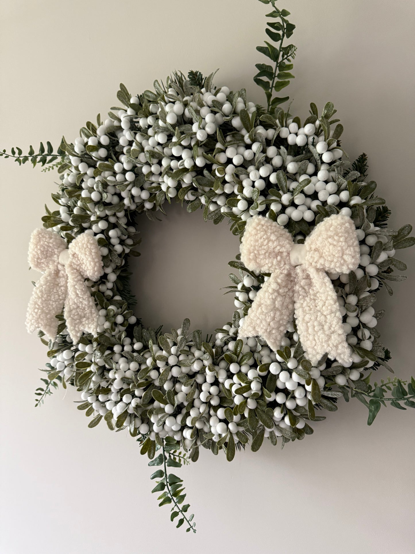 Decorative wreath with white berries and boucle bows on a plain background