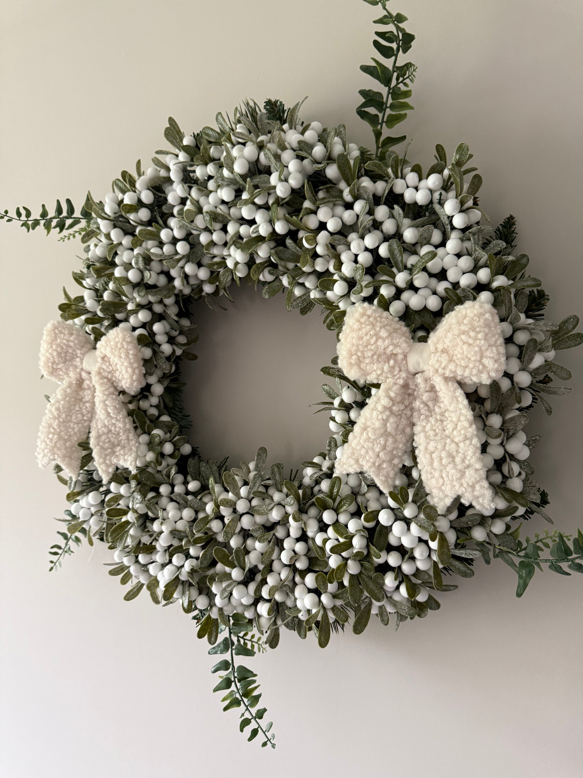 Decorative wreath with white berries and boucle bows on a plain background