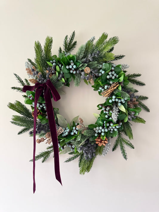 Decorative wreath with greenery and a burgundy ribbon on a beige background