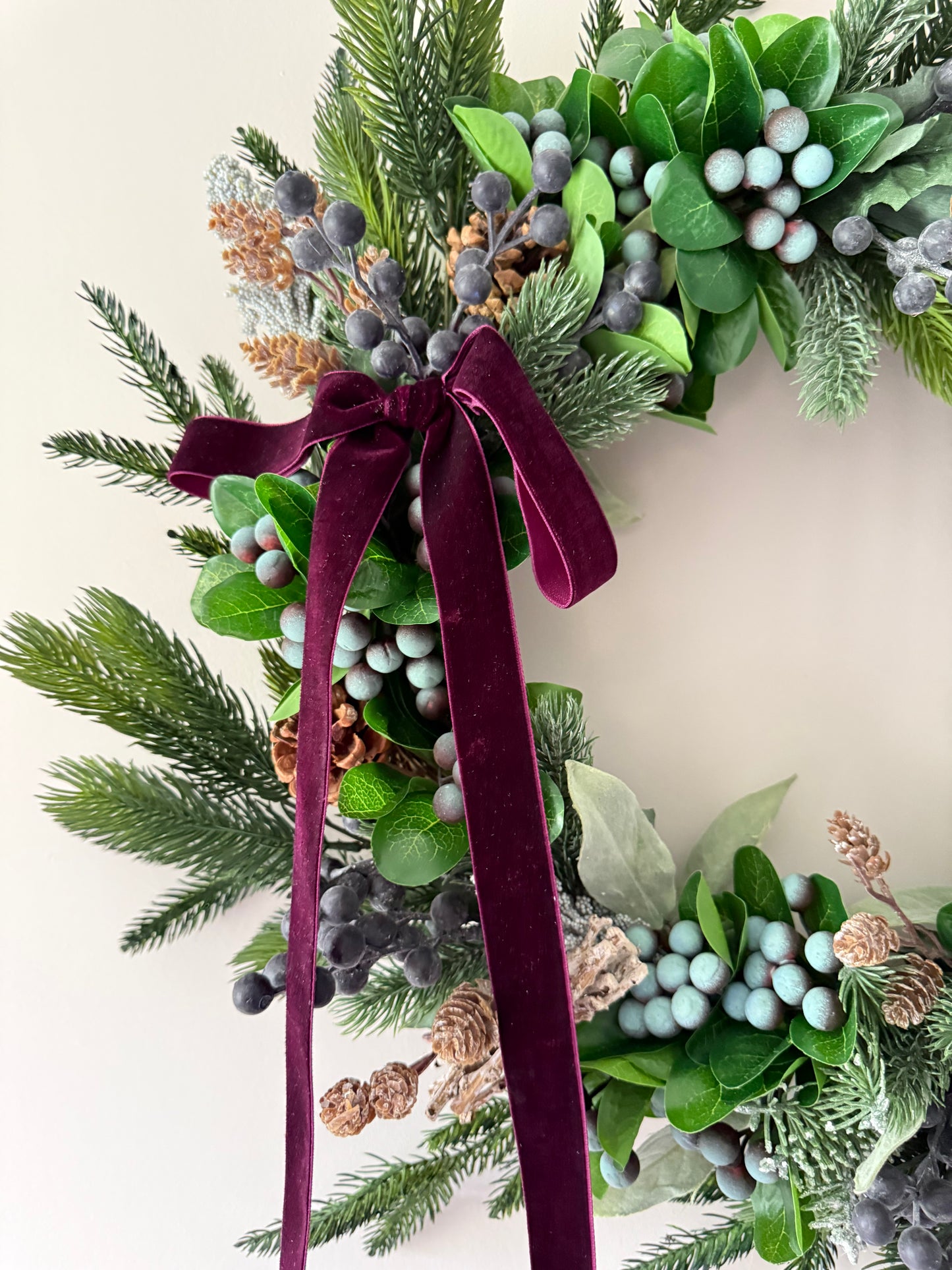 Decorative wreath with greenery, berries, and a burgundy ribbon on a light background