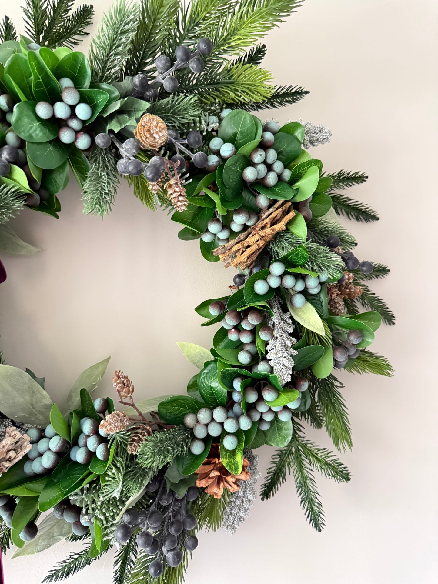 Decorative wreath with greenery, berries, and pinecones on a neutral background
