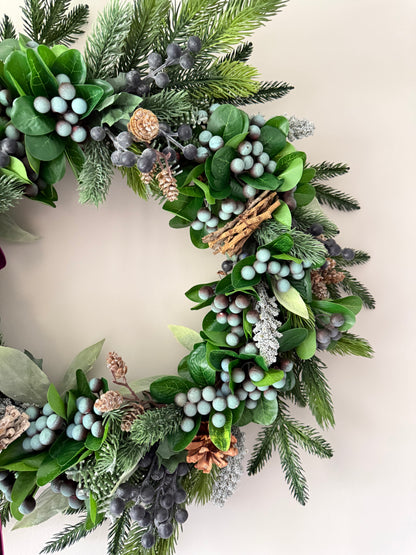 Decorative wreath with greenery, berries, and pinecones on a neutral background
