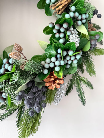 Decorative wreath with greenery, berries, and pinecones on a neutral background