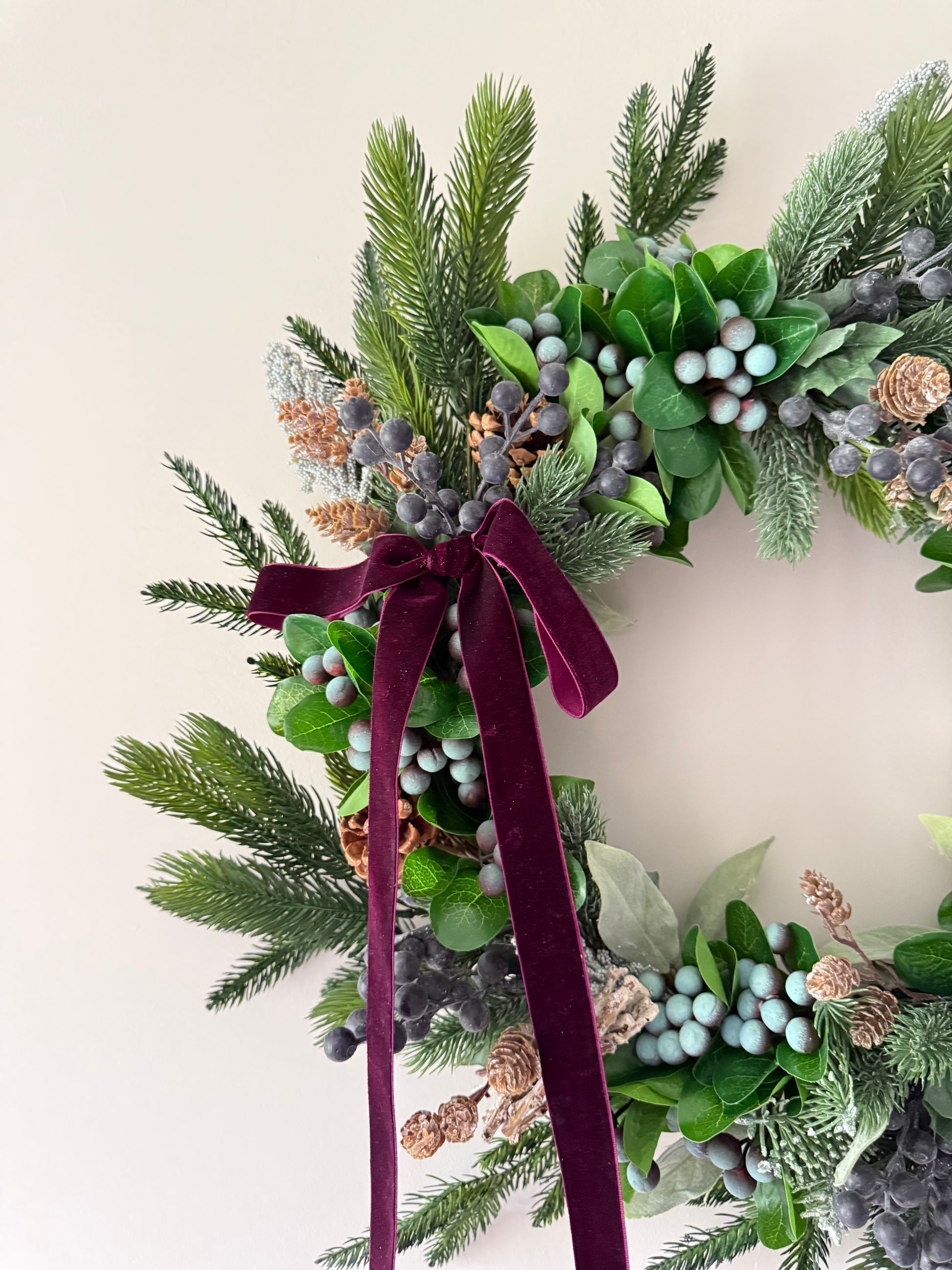 Decorative wreath with greenery, berries, and a purple ribbon on a light background