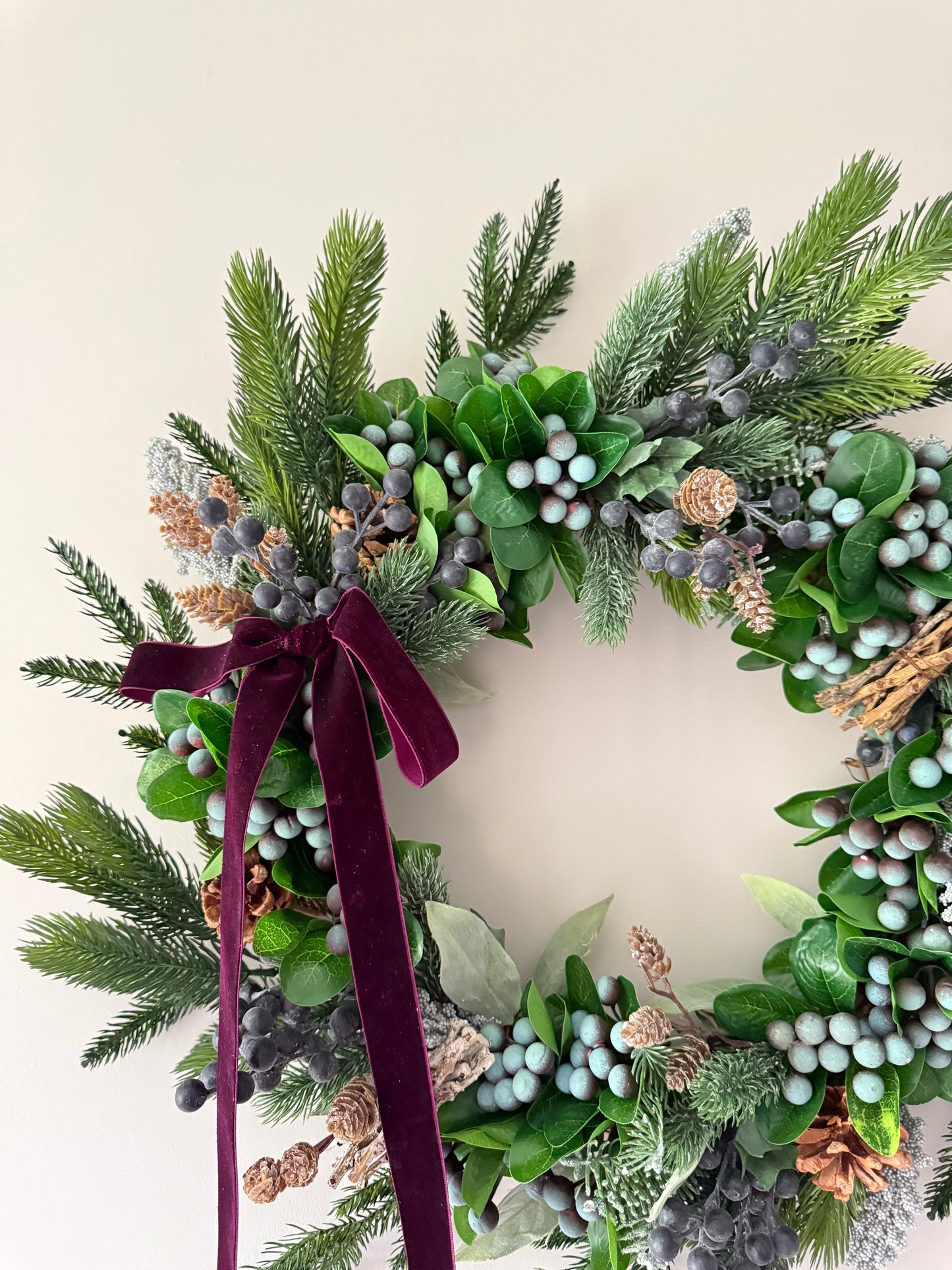 Decorative wreath with greenery, berries, and a burgundy ribbon on a light background