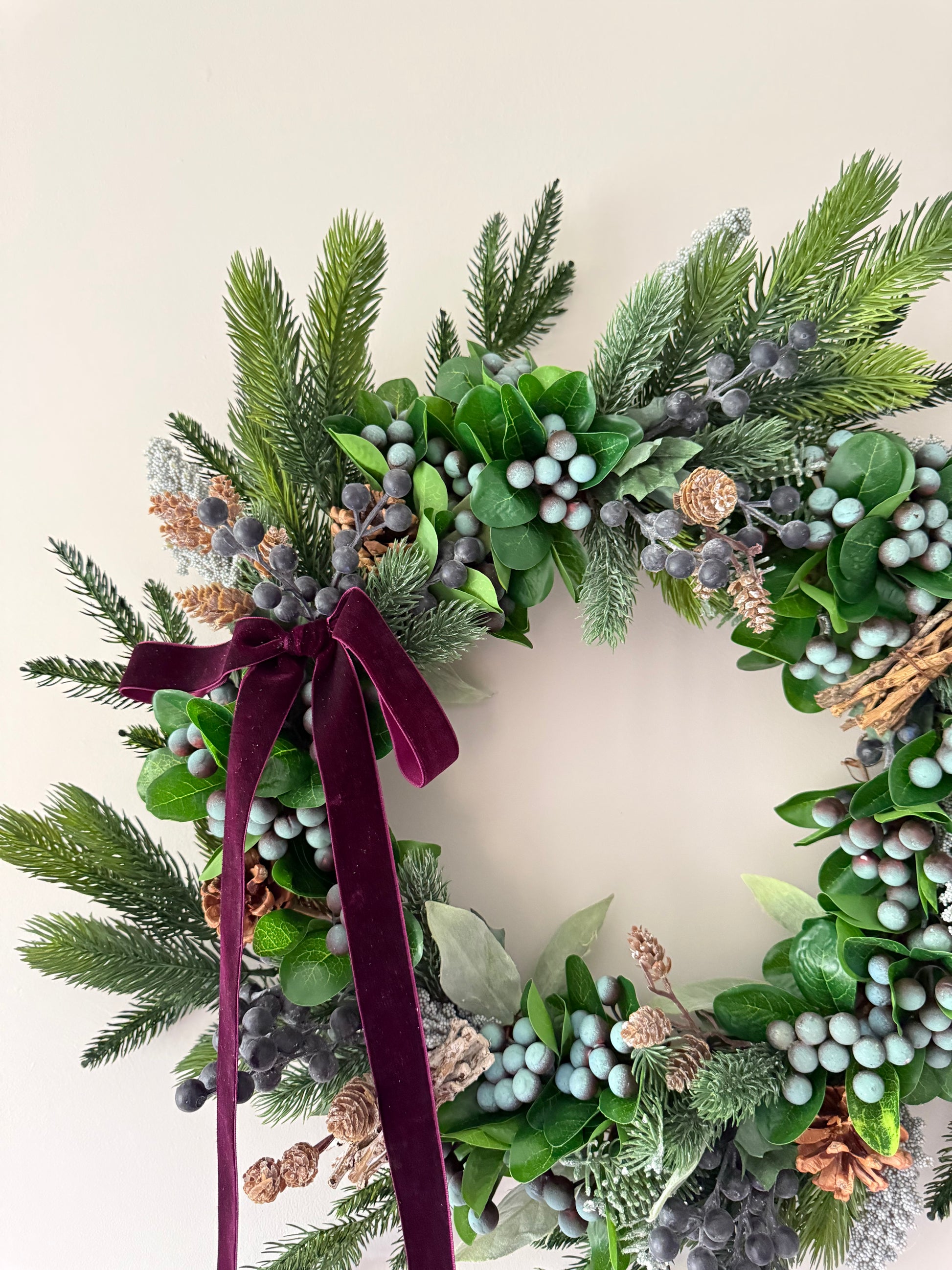 Decorative wreath with greenery, berries, and a burgundy ribbon on a light background