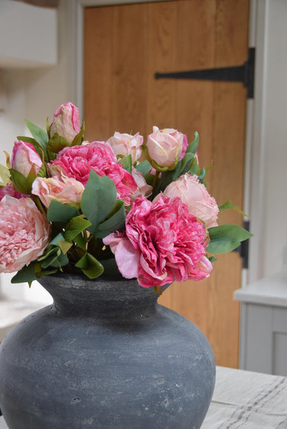 Grey antique vase placed on kitchen counter top with an arrangement of pale pink and hot pink peonies. Arranged in a country style kitchen for home decor.