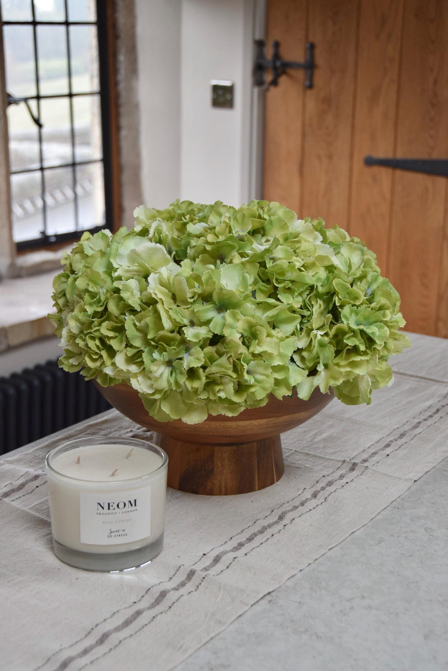 Wooden footed chalice bowl placed on a kitchen counter top with an arrangement of green hydrangeas. Displayed in a country style kitchen for home decor.