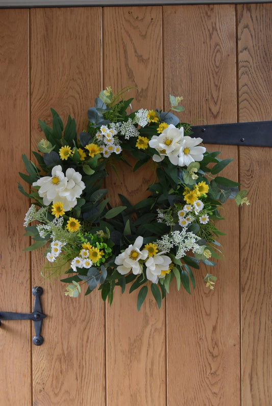 Wreath hanging on rustic country style wooden door with a mixture of daisies, wildflowers, mini bud sprays and greenery. Displayed on a barn door for home decor.