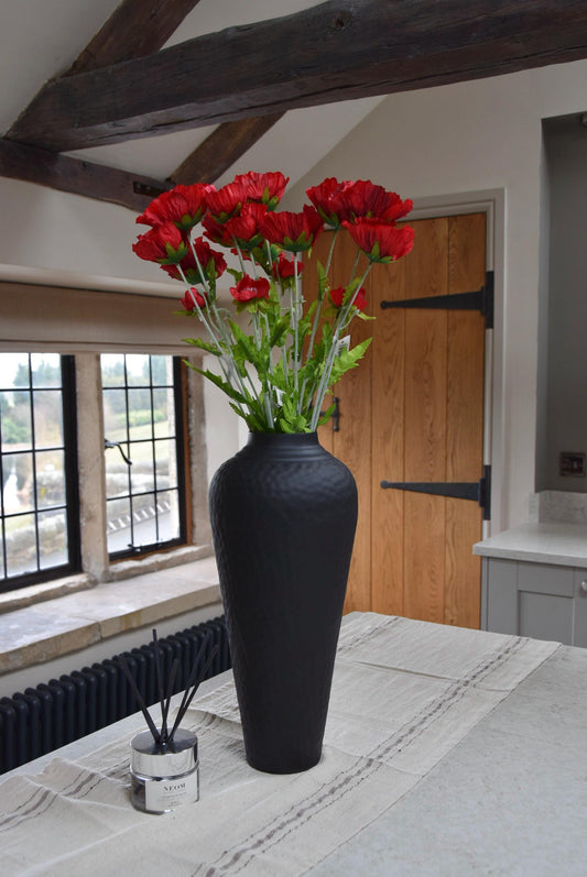 Tall black vase placed on a kitchen countertop with a bunch of tall red country poppies. Displayed in a country style kitchen for home decor.