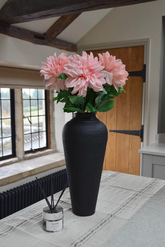 Tall black vase placed on a kitchen countertop with a bunch of pink monarch dahlia stems. Displayed in a country style kitchen for home decor.