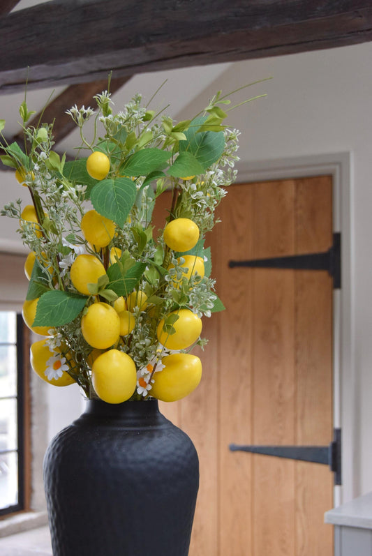 Tall black vase placed on a kitchen countertop with a bunch of faux lemon branches. Displayed in a country style kitchen for home decor.