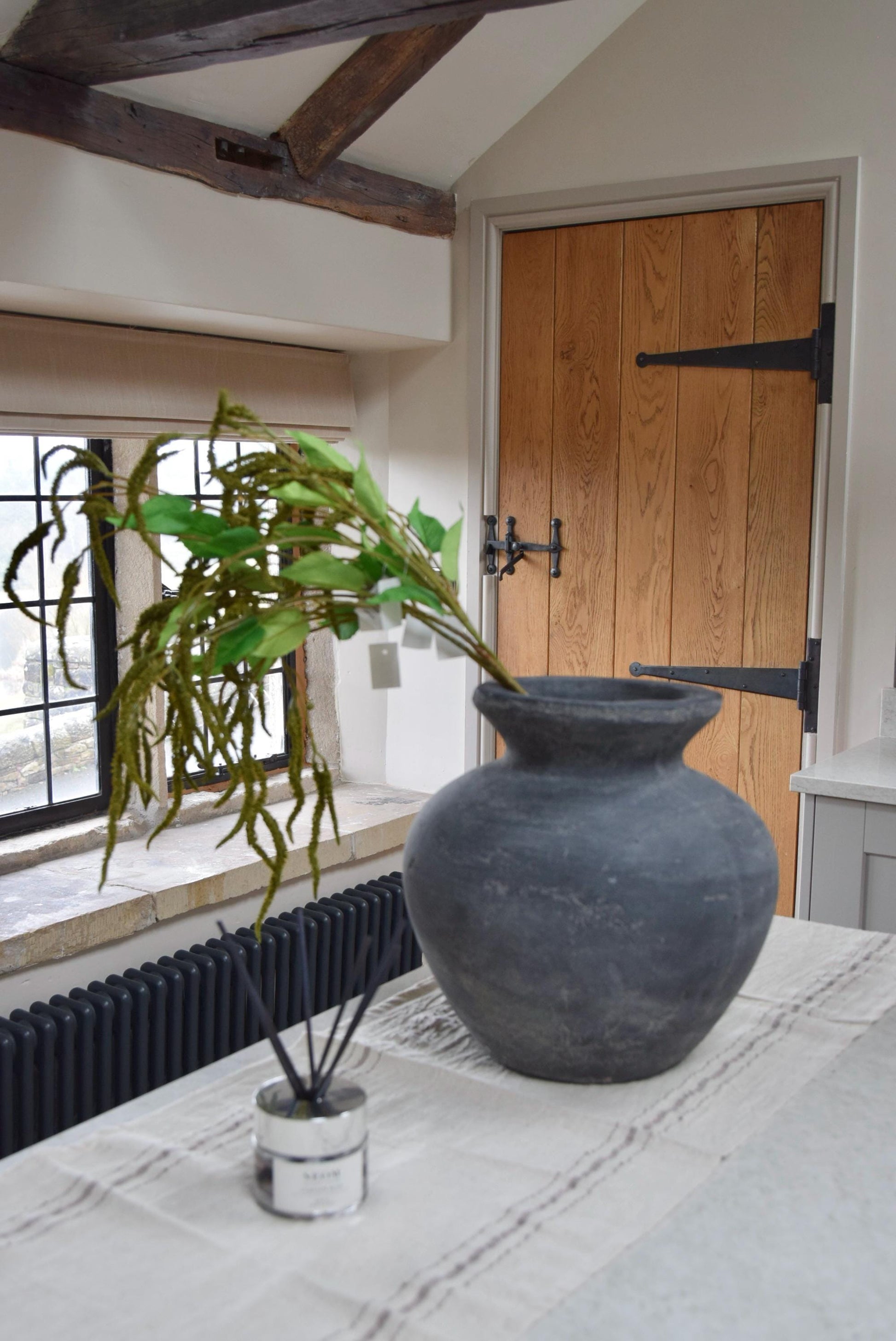 Grey vase placed on a kitchen countertop with bunch of artificial green catkin stems. Displayed in a country style kitchen for home decor.