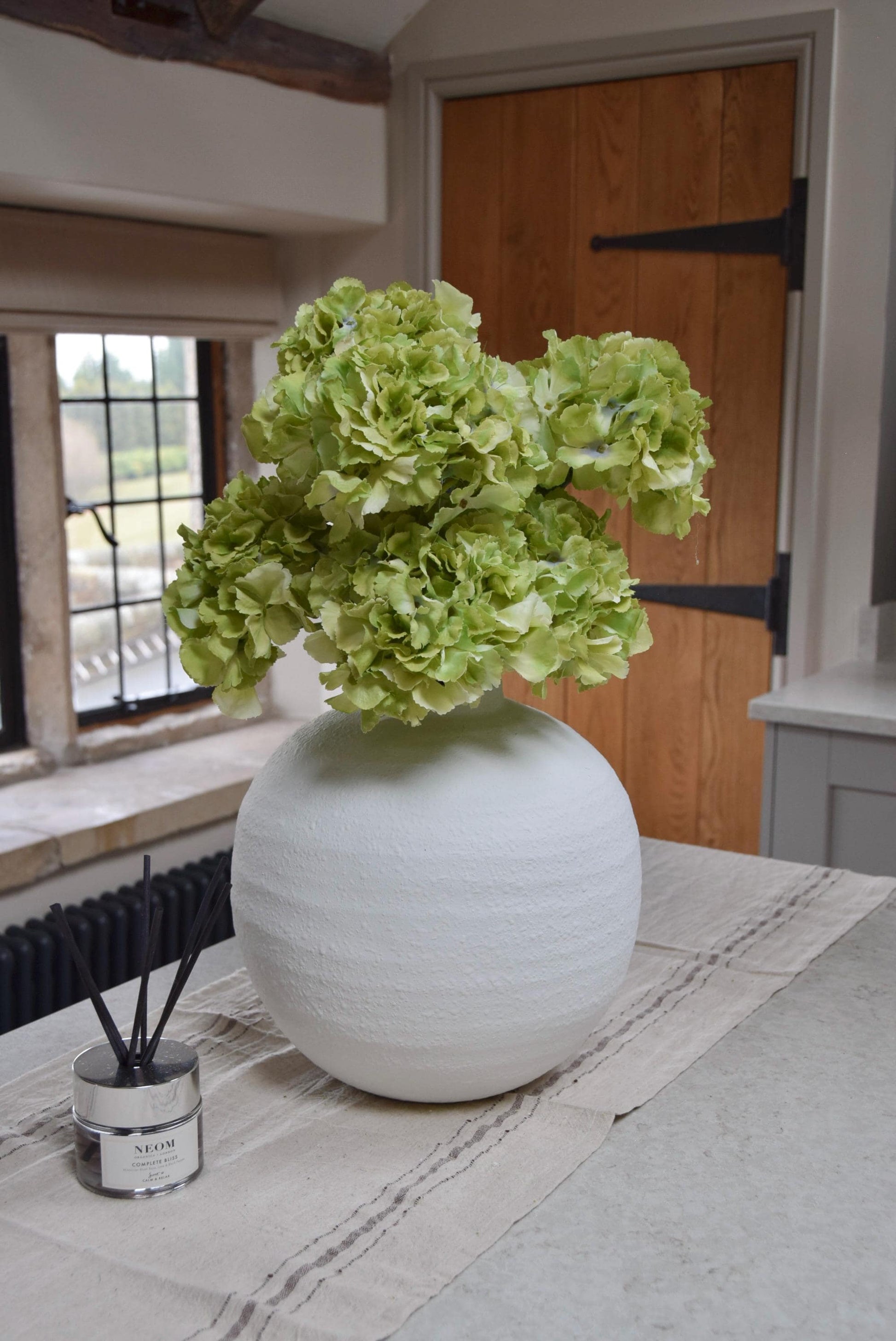 White round vase on kitchen countertop featuring green hydrangeas. Displayed in a country style kitchen for home decor.