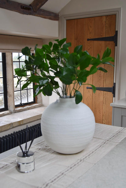White round vase placed on a kitchen countertop with a bunch of obovate leaf foliage stems. Displayed in a country style kitchen for home decor.