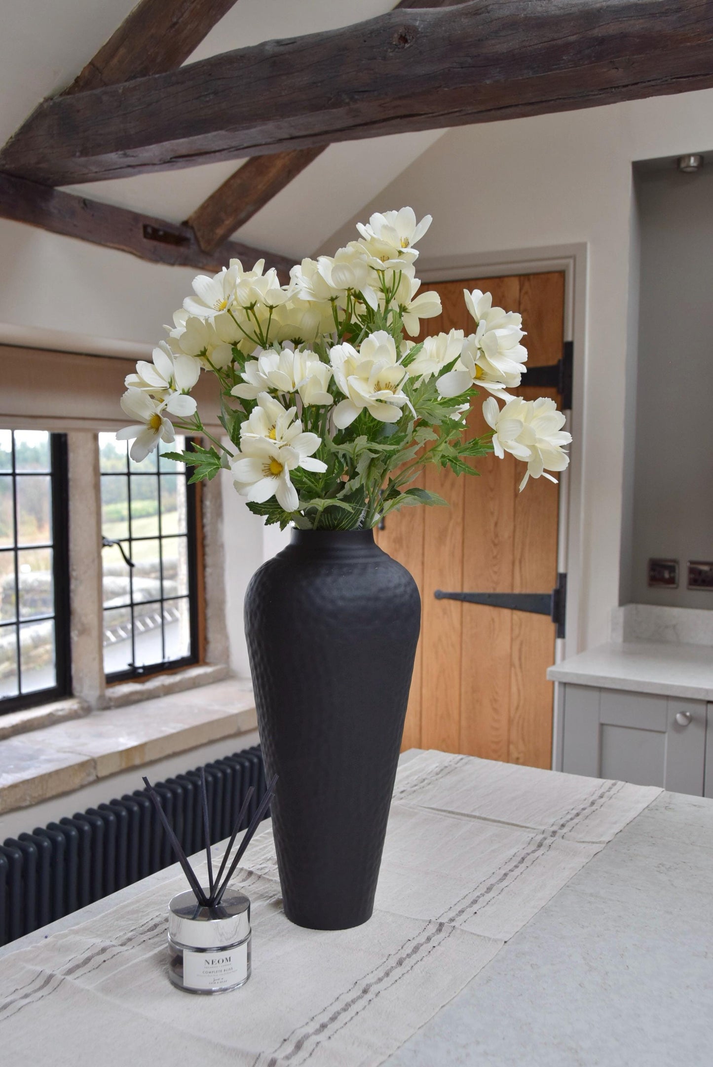 Tall black vase with cream wildflowers placed on a kitchen countertop in a country style kitchen for home decor.
