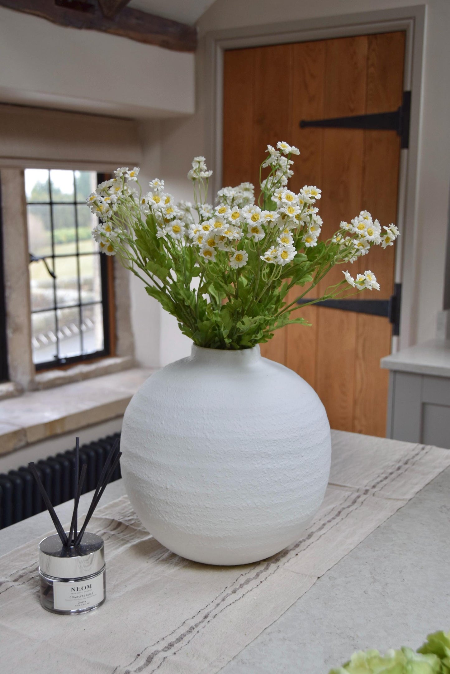 White round vase placed on a kitchen countertop with a bunch of daisies displayed in a country style kitchen for home decor.