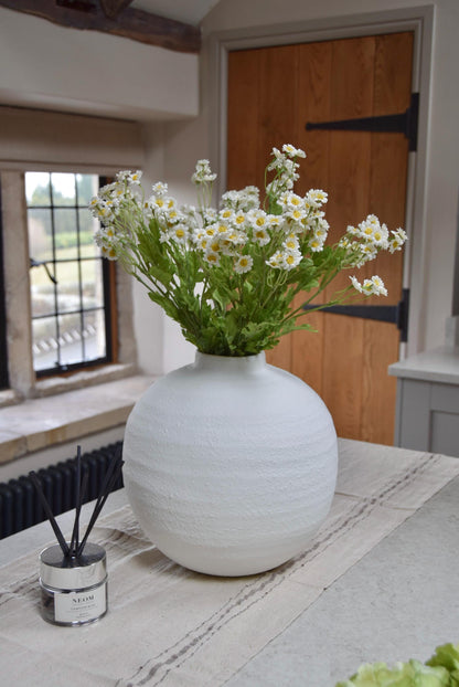 White round vase placed on a kitchen countertop with a bunch of daisies displayed in a country style kitchen for home decor.