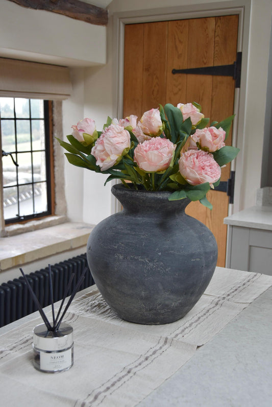 Grey vase placed on a kitchen countertop with a lovely bunch of pale pink peonies. Displayed in a country style kitchen for home decor.
