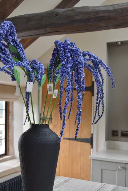 Tall black vase on a kitchen countertop with long purple amaranthus trailing stems. Set in a country style kitchen for home decor.