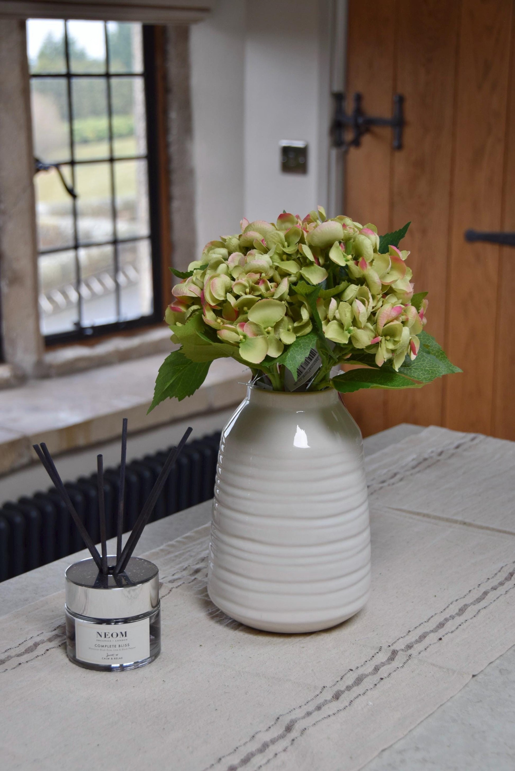 Mini green Hydrangeas in a small cream vase sat on a kitchen countertop in a country style house for home decor.