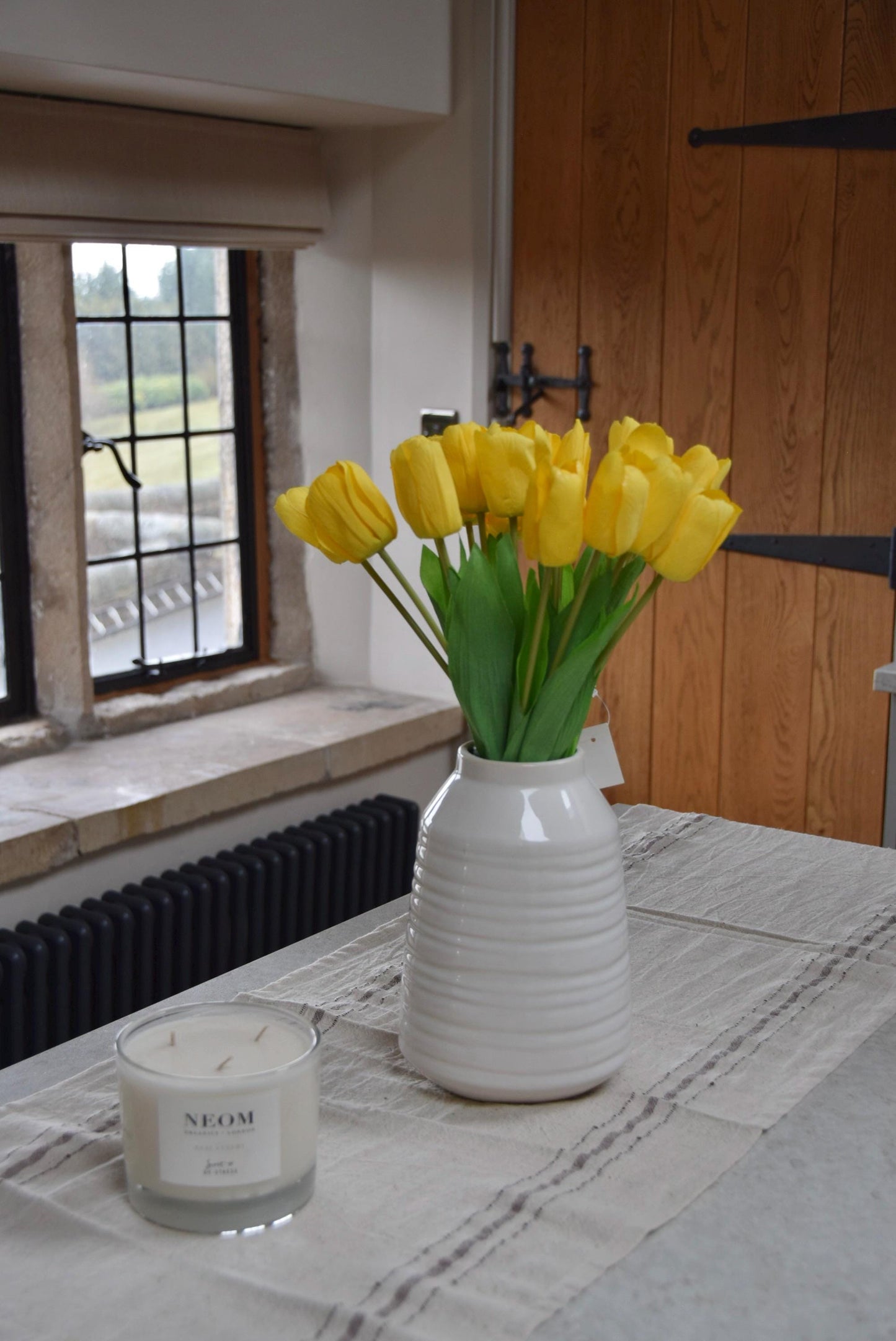 Yellow tulips set in a cream vase on a kitchen counter top in a country style kitchen for home decor