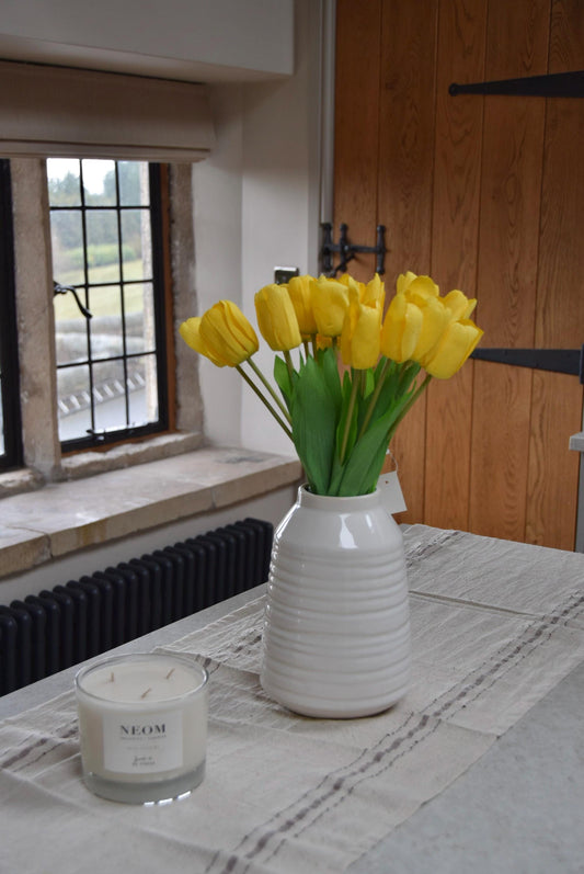 Yellow tulips set in a cream vase on a kitchen counter top in a country style kitchen for home decor
