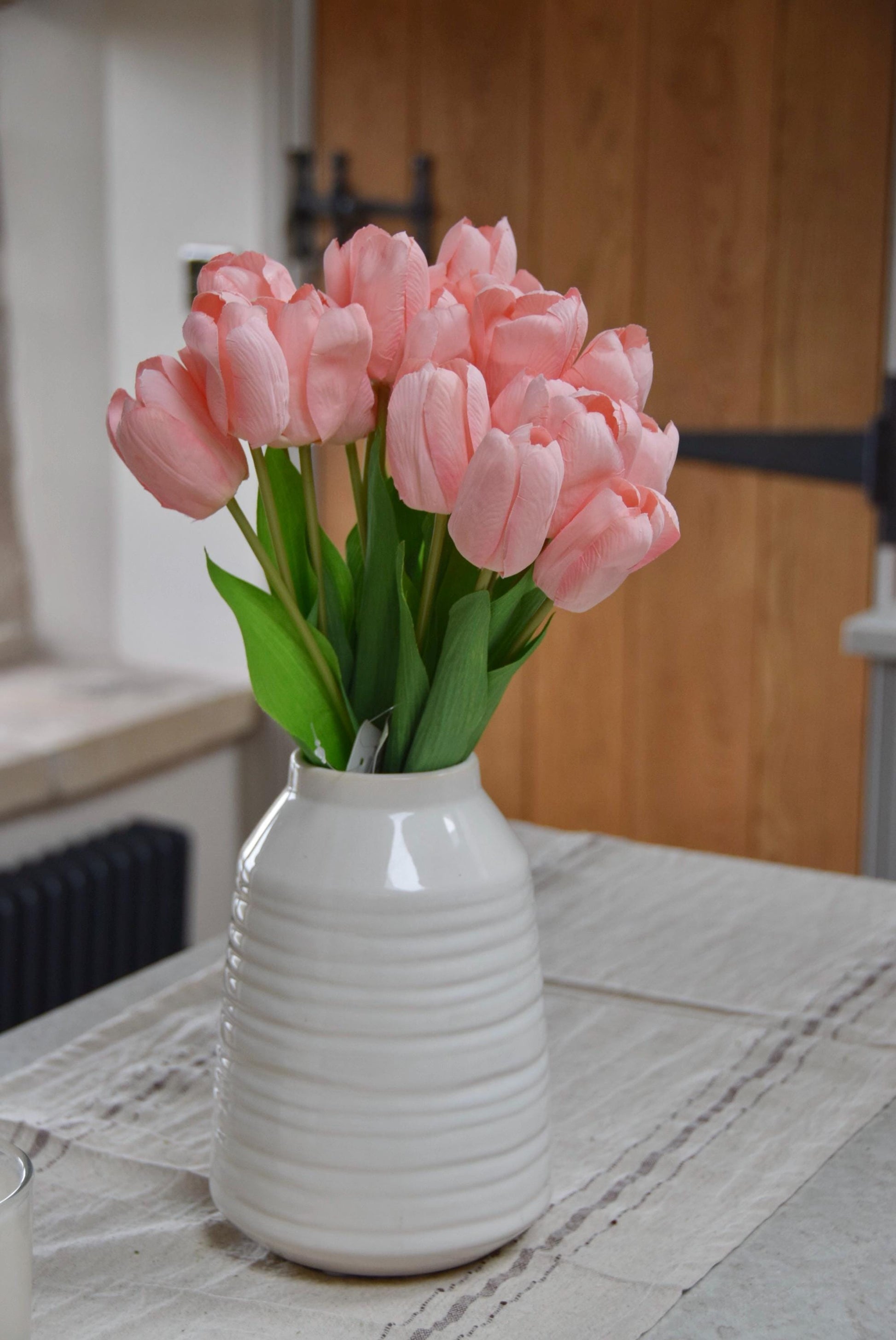 Pink tulips set in a cream vase on a kitchen counter top in a country style kitchen for home decor