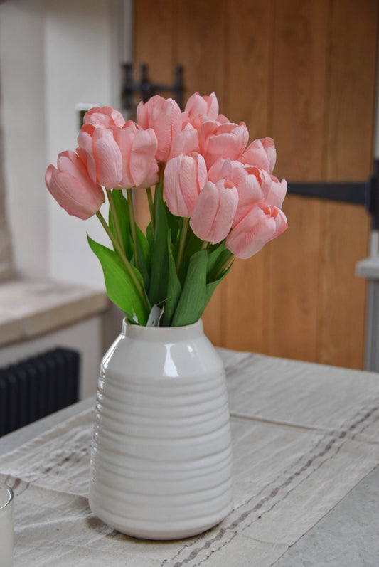 Pink tulips set in a cream vase on a kitchen counter top in a country style kitchen for home decor