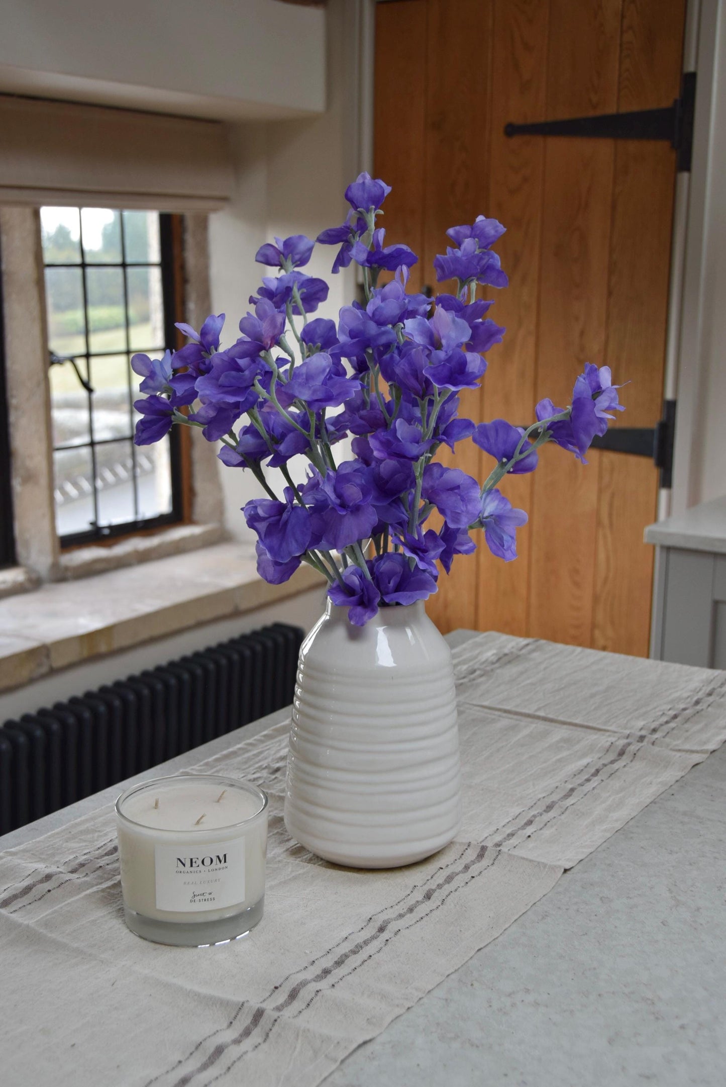Purple sweet peas set in a cream vase on a kitchen countertop in a country style house for home decor.