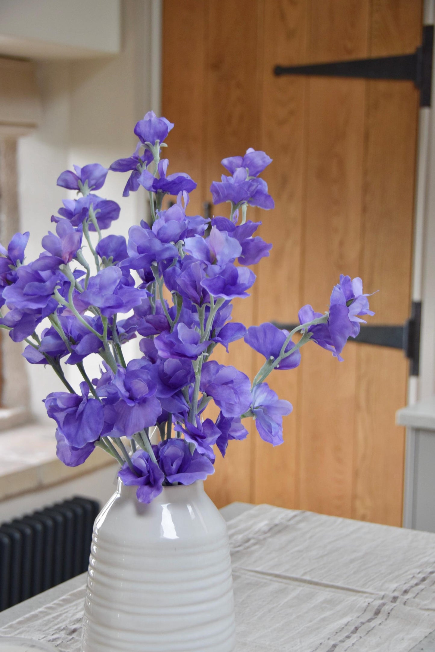 Purple sweet peas set in a cream vase on a kitchen countertop in a country style house for home decor.