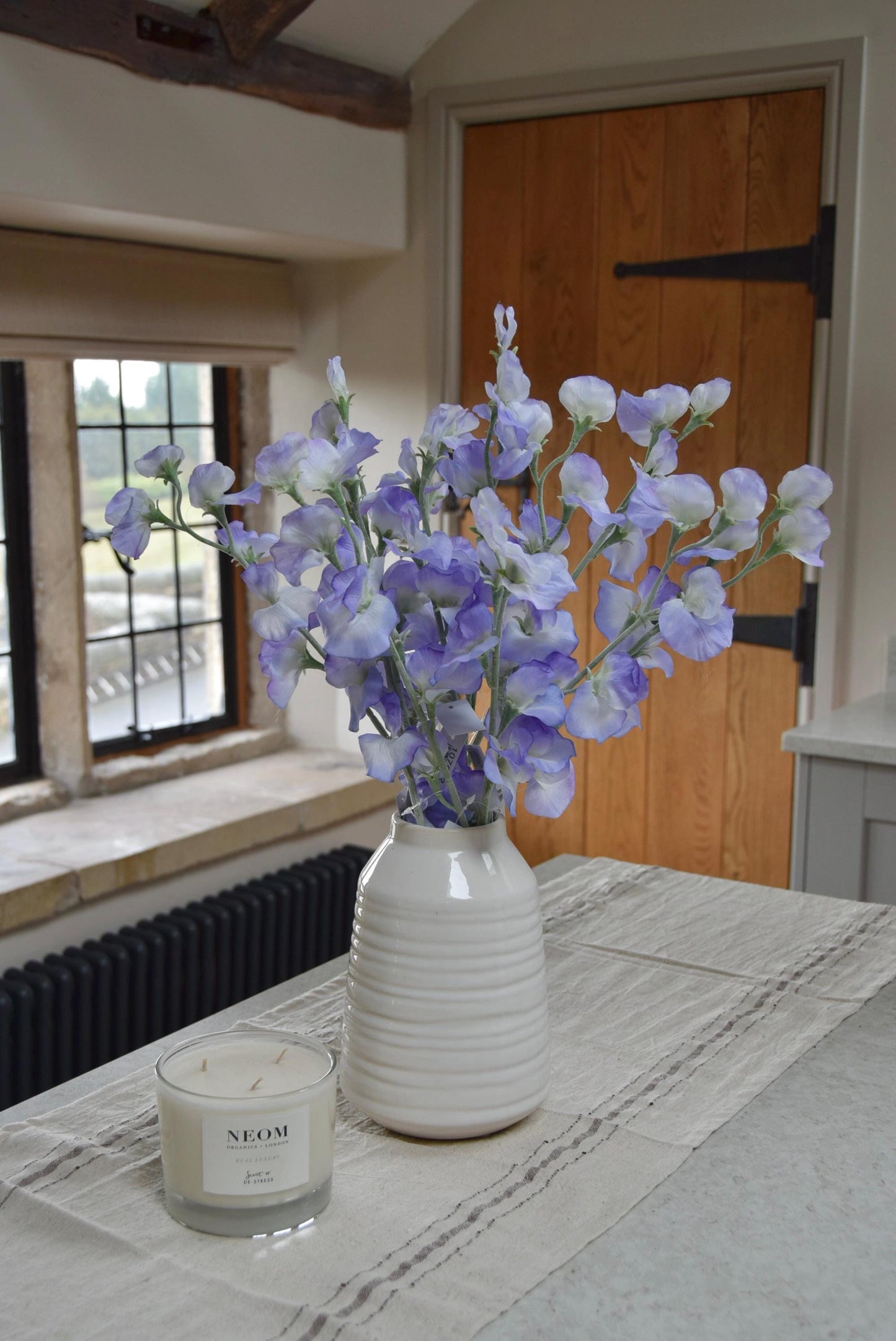 Lilac sweet peas set in a cream vase on a kitchen countertop in a country style house for home decor.
