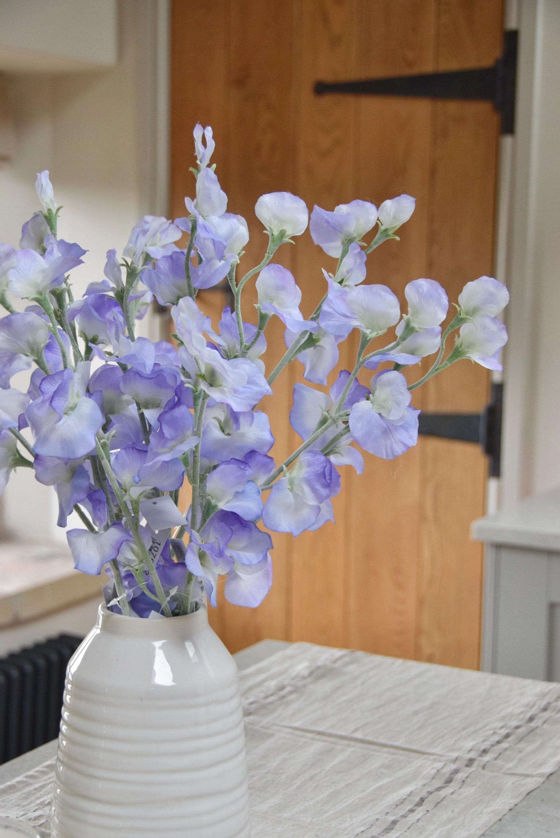 Lilac sweet peas set in a cream vase on a kitchen countertop in a country style house for home decor.