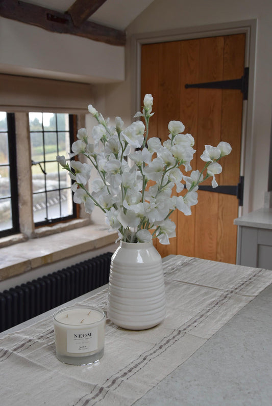 White sweet peas set in a cream vase on a kitchen countertop in a country style house for home decor.